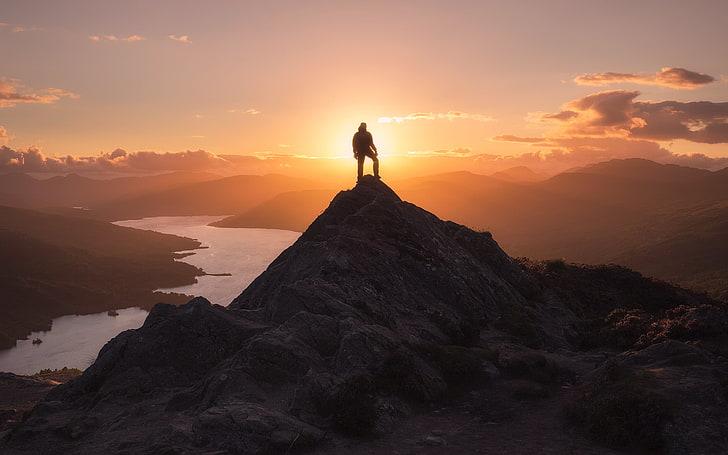 silhuetti vuoresta, jonka päällä seisoo ihminen ja taustalla auringonlasku